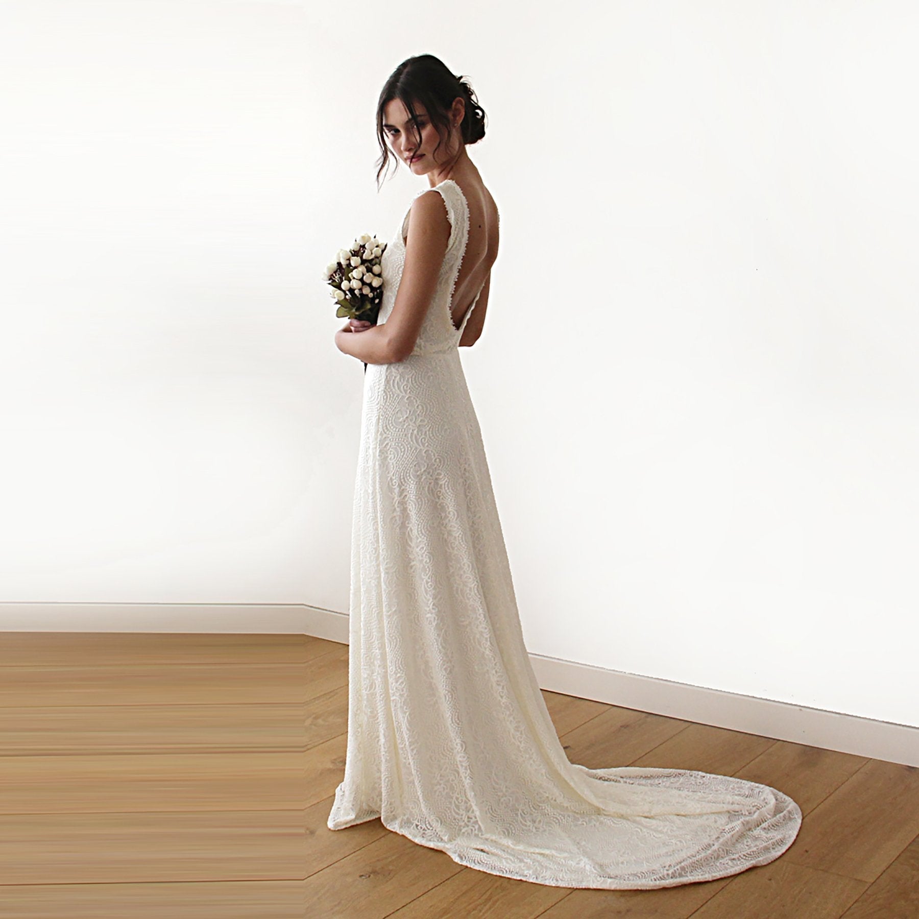 Bride in sleeveless lace wedding dress with train, holding bouquet, showcasing vintage elegance and modern style.