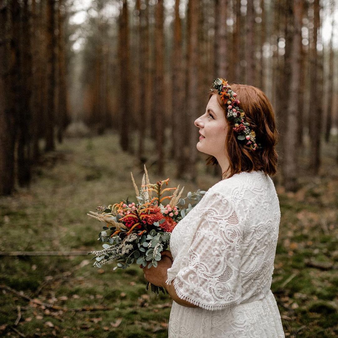 Woman in lace gown with butterfly sleeves holding bouquet in forest setting