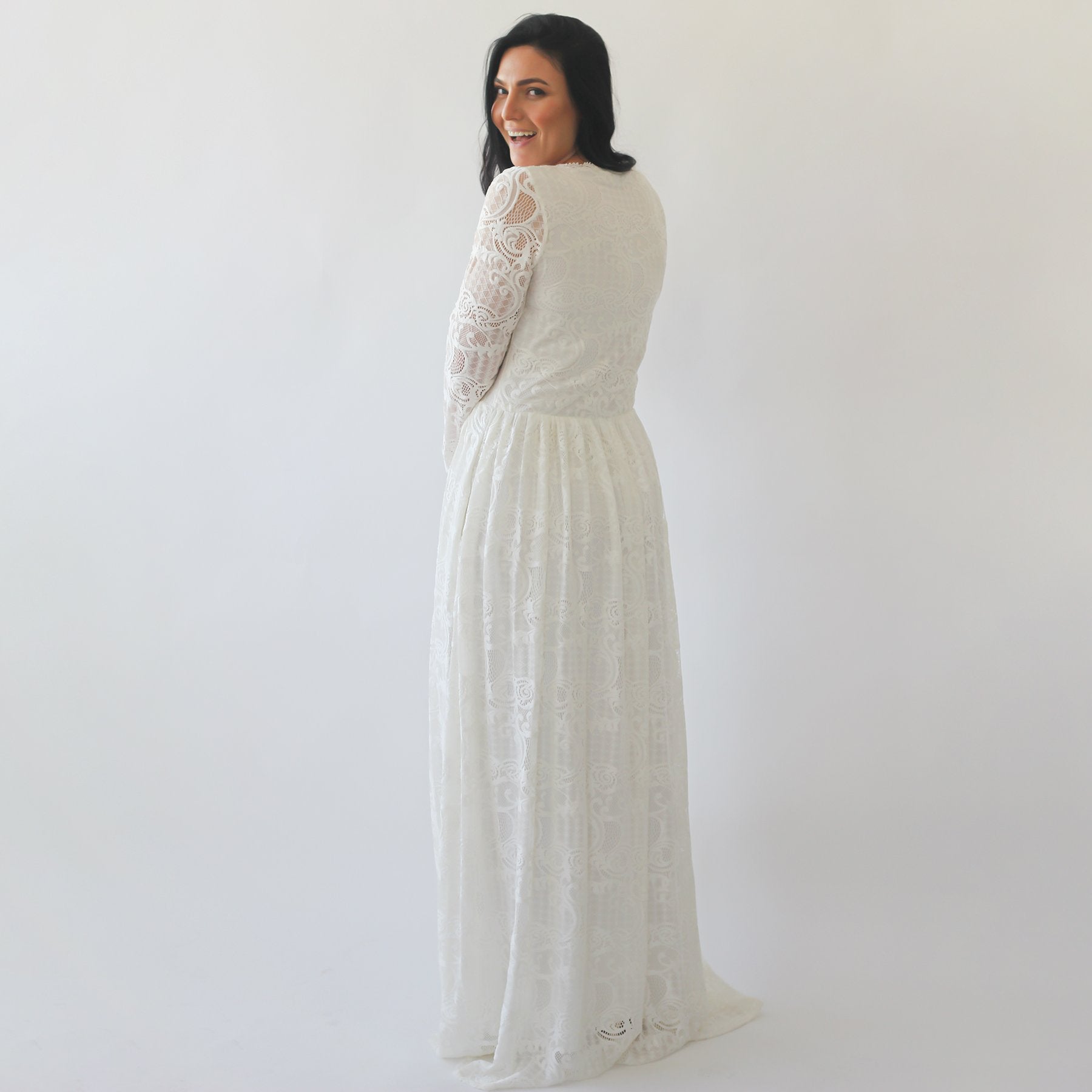 Woman wearing Nirelda ivory lace wedding dress with square neck and sheer long sleeves, showing back view with elegant drape.