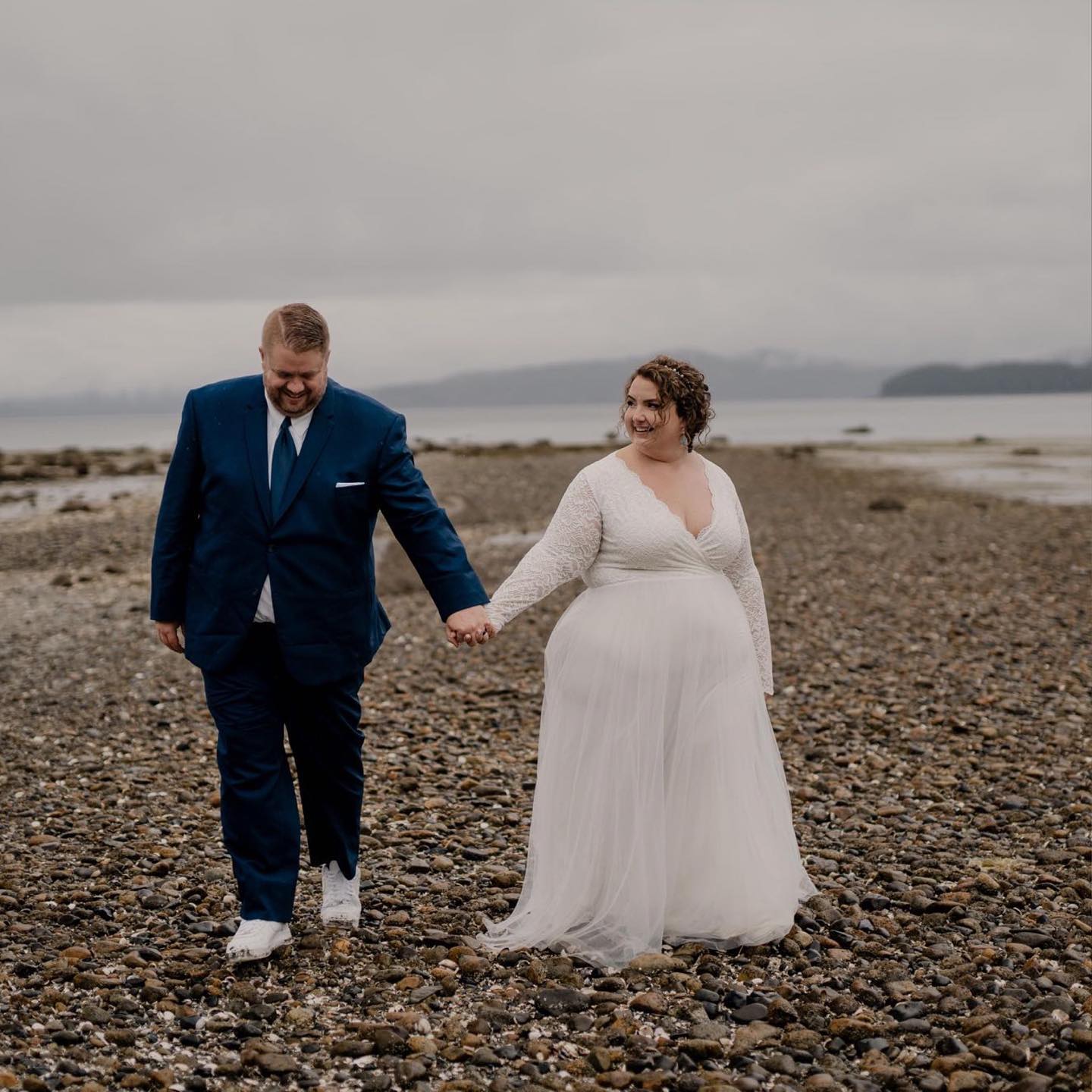Bride in Celestielle Grace Wedding Dress with groom walking on rocky beach.