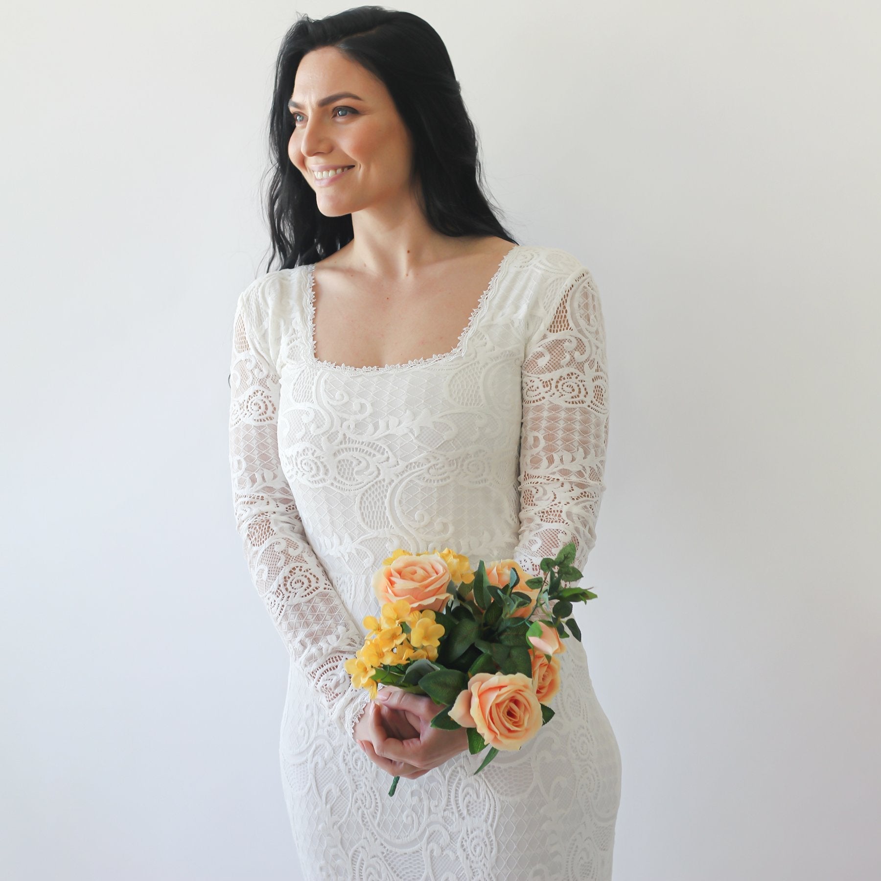 Woman in Elirelle ivory lace wedding dress with sleeves holding bouquet, showcasing elegant mermaid silhouette and square neckline.