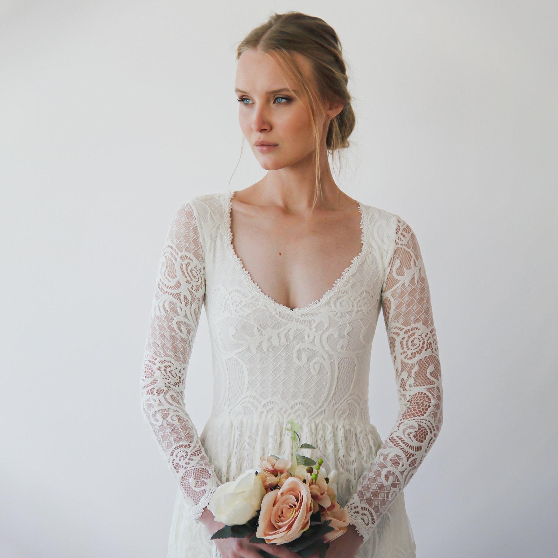 Bride wearing Auremine Diamond Neck Wedding Gown with lace sleeves holding a bouquet, highlighting elegant design with modern pockets.