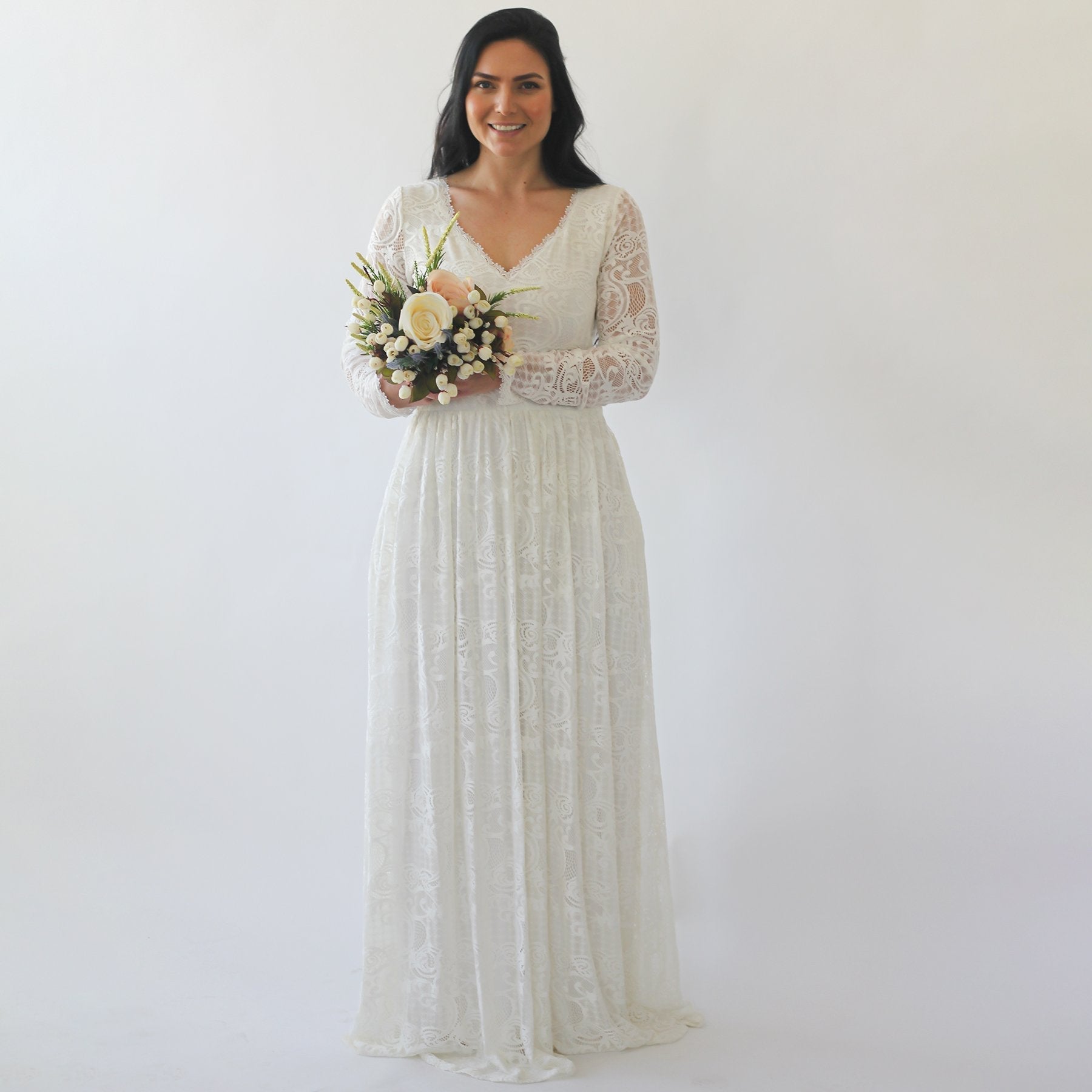 Bride wearing Auremine wedding gown with lace sleeves, diamond neckline, and skirt with pockets, holding a bouquet of flowers.