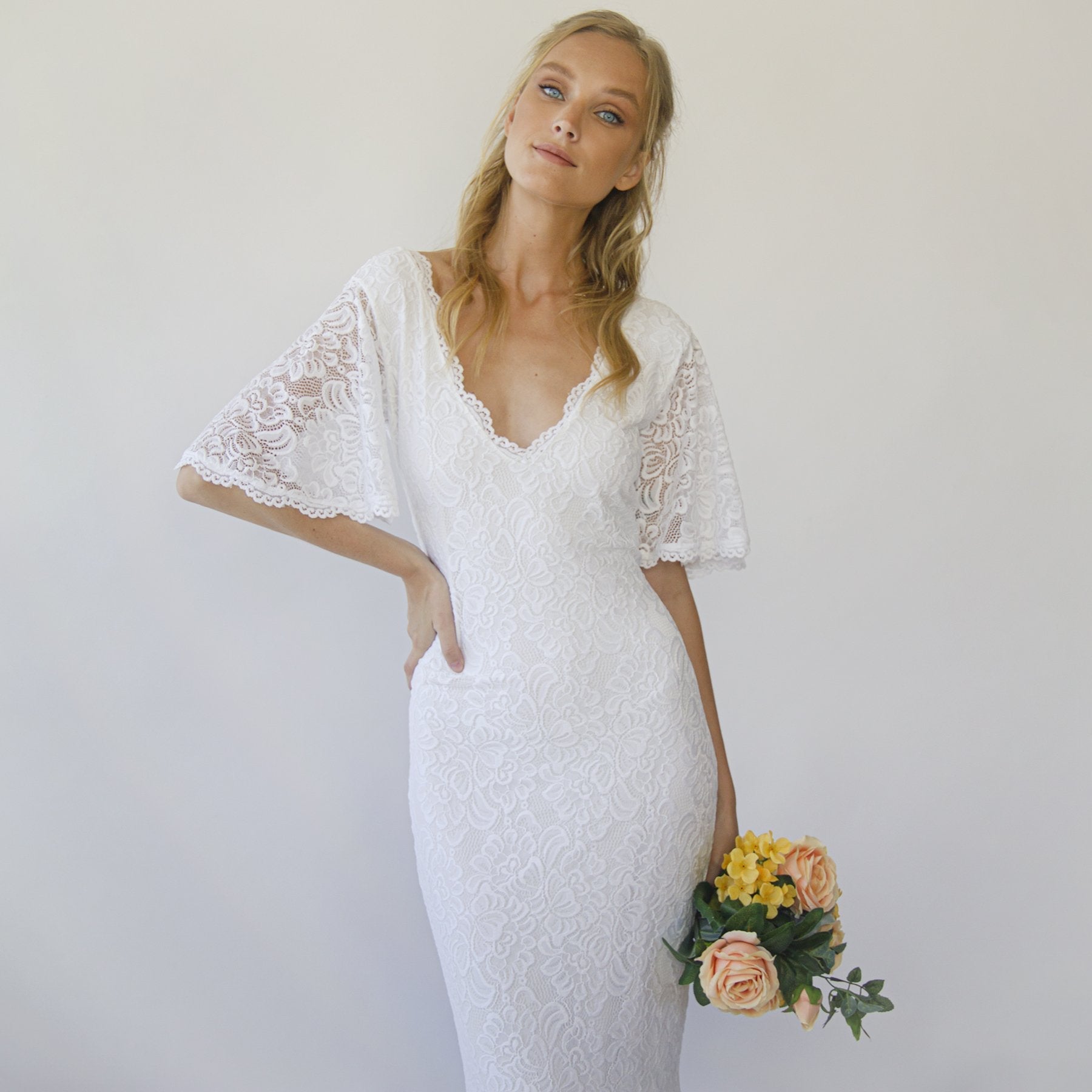 Bride in Elvenya Boho Sheath Wedding Dress with lace, V-neckline, and butterfly sleeves holding a bouquet of flowers.