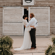 Bride in ivory lace two-piece wedding dress with bell sleeves embraces groom in rustic outdoor setting.