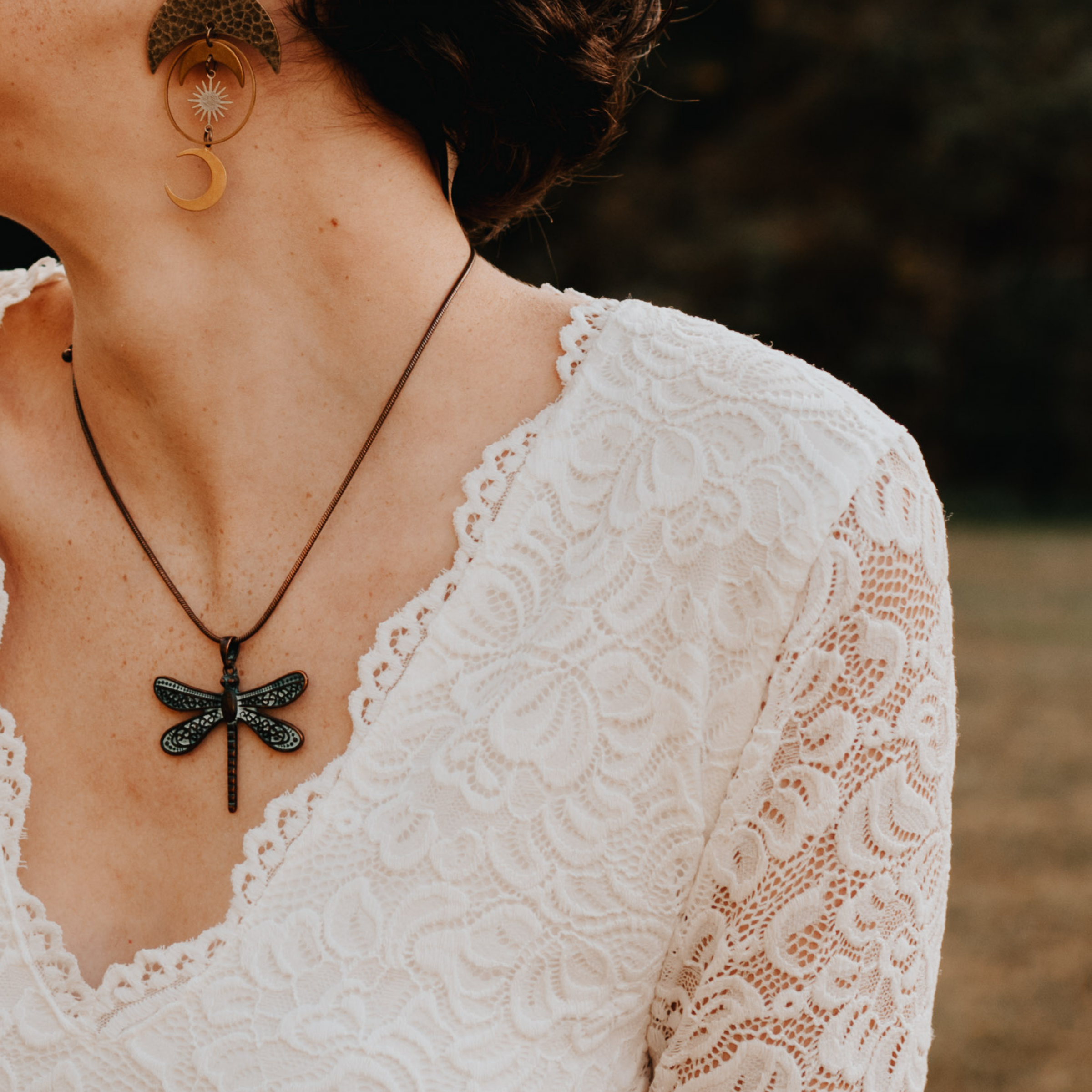 Close-up of ivory lace top with dragonfly necklace, showcasing intricate lace detail and bohemian elegance.