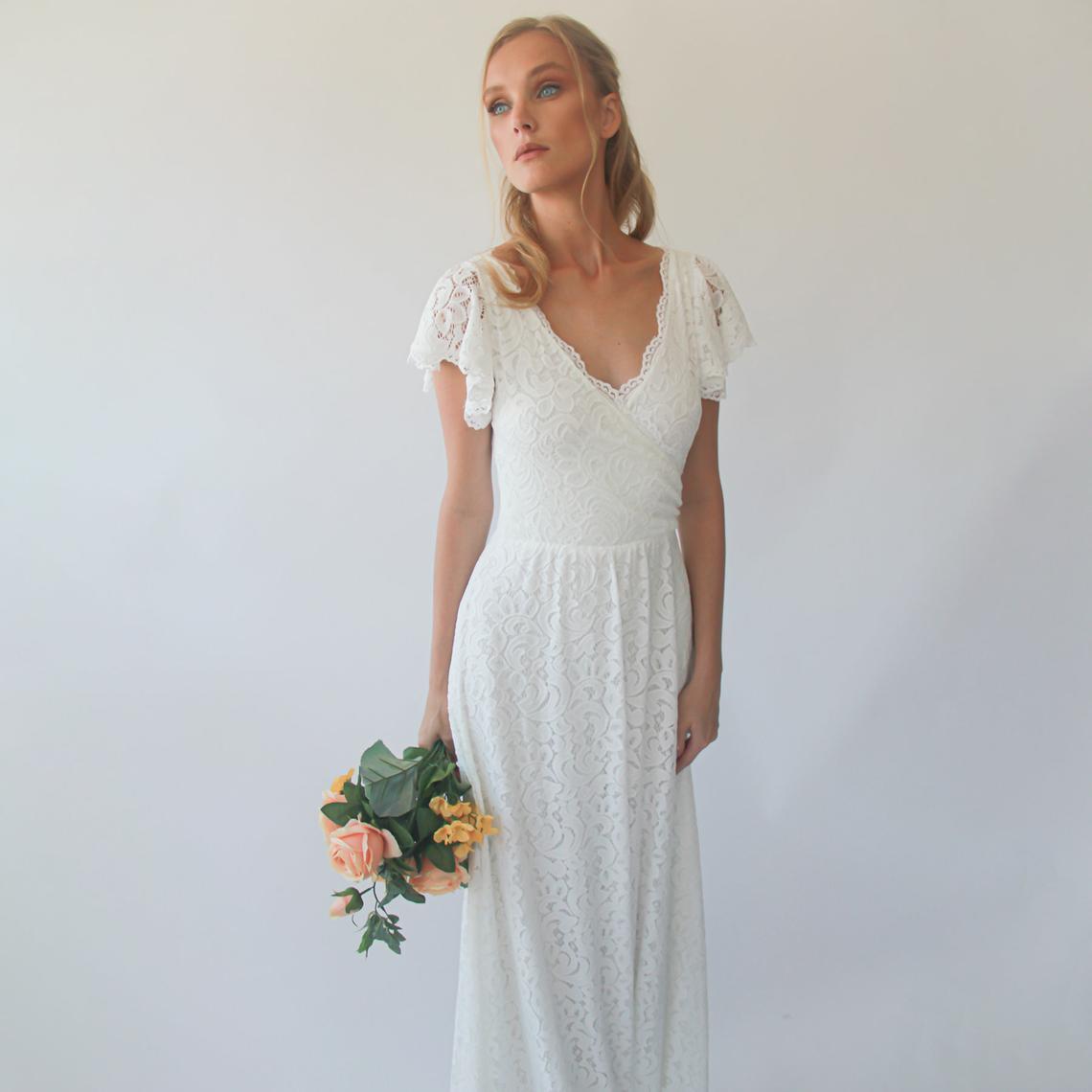 Woman in ivory Elowen Lace Wrap Wedding Gown holding a bouquet, featuring cap sleeves and floor-length silhouette.