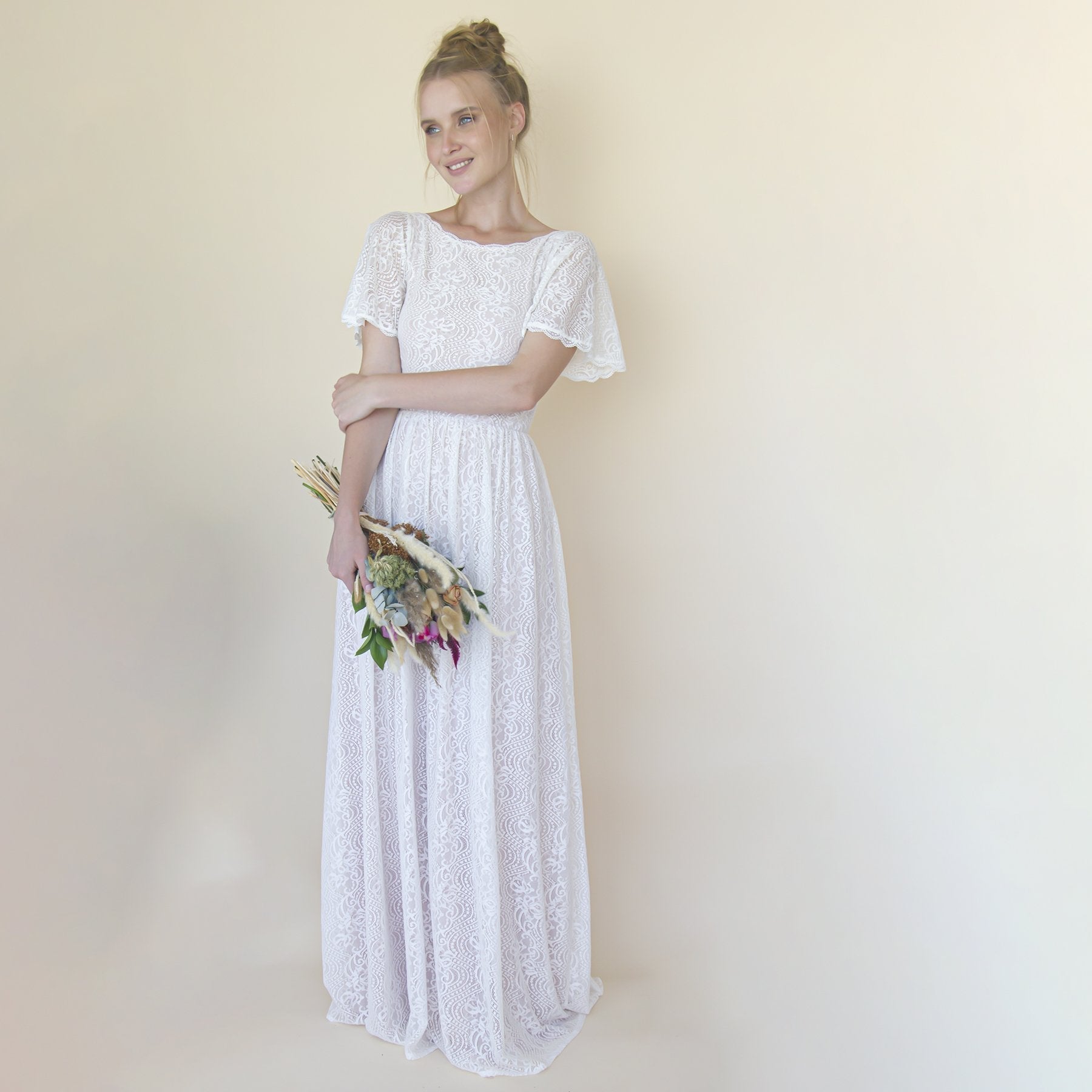 Bride wearing Maerelle Vintage Lace Wedding Gown with flutter sleeves, holding bouquet; ivory lace over blush lining, elegant style.