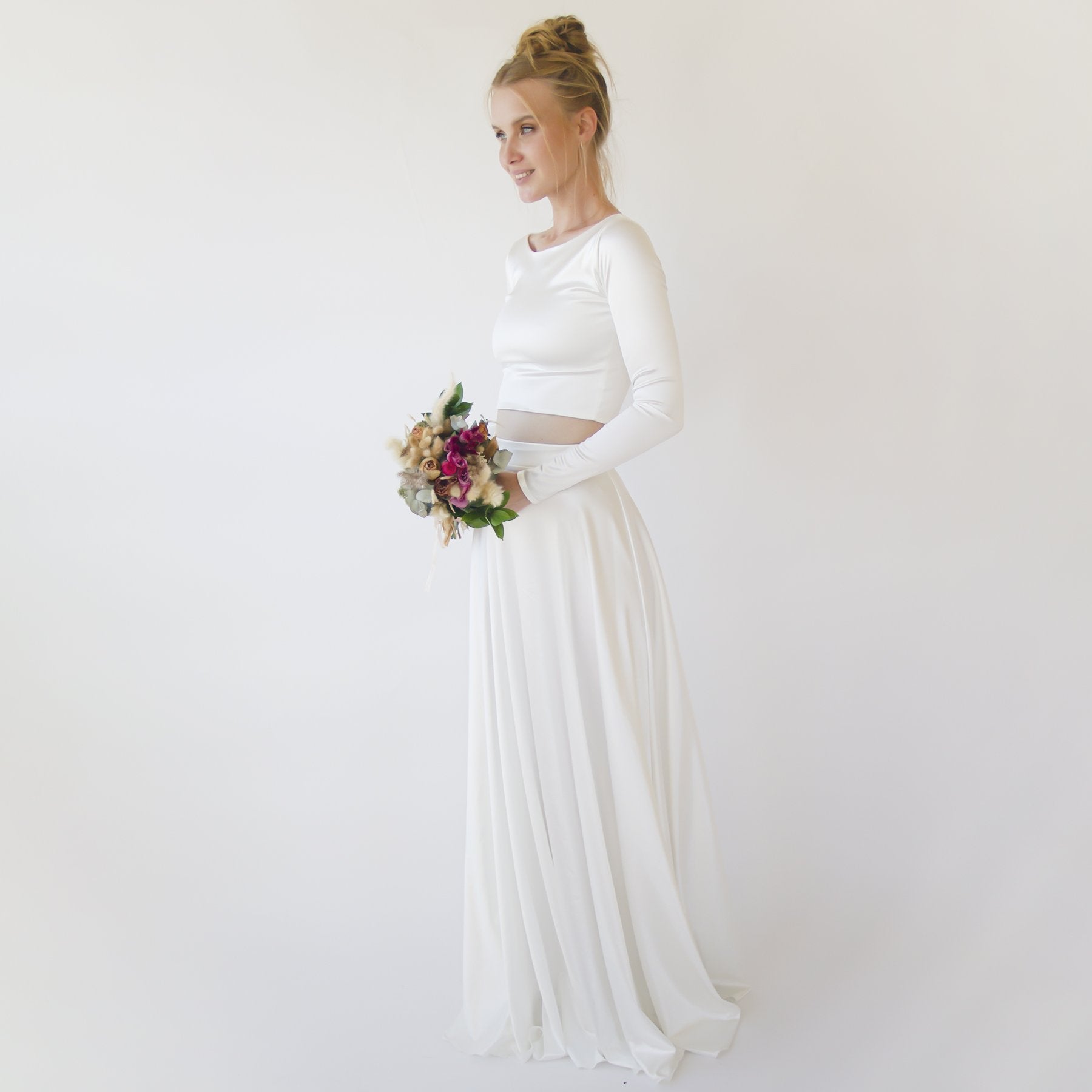 Bride wearing Silvanya Satin Two-Piece Wedding Dress with long sleeves holding a bouquet against a white background.