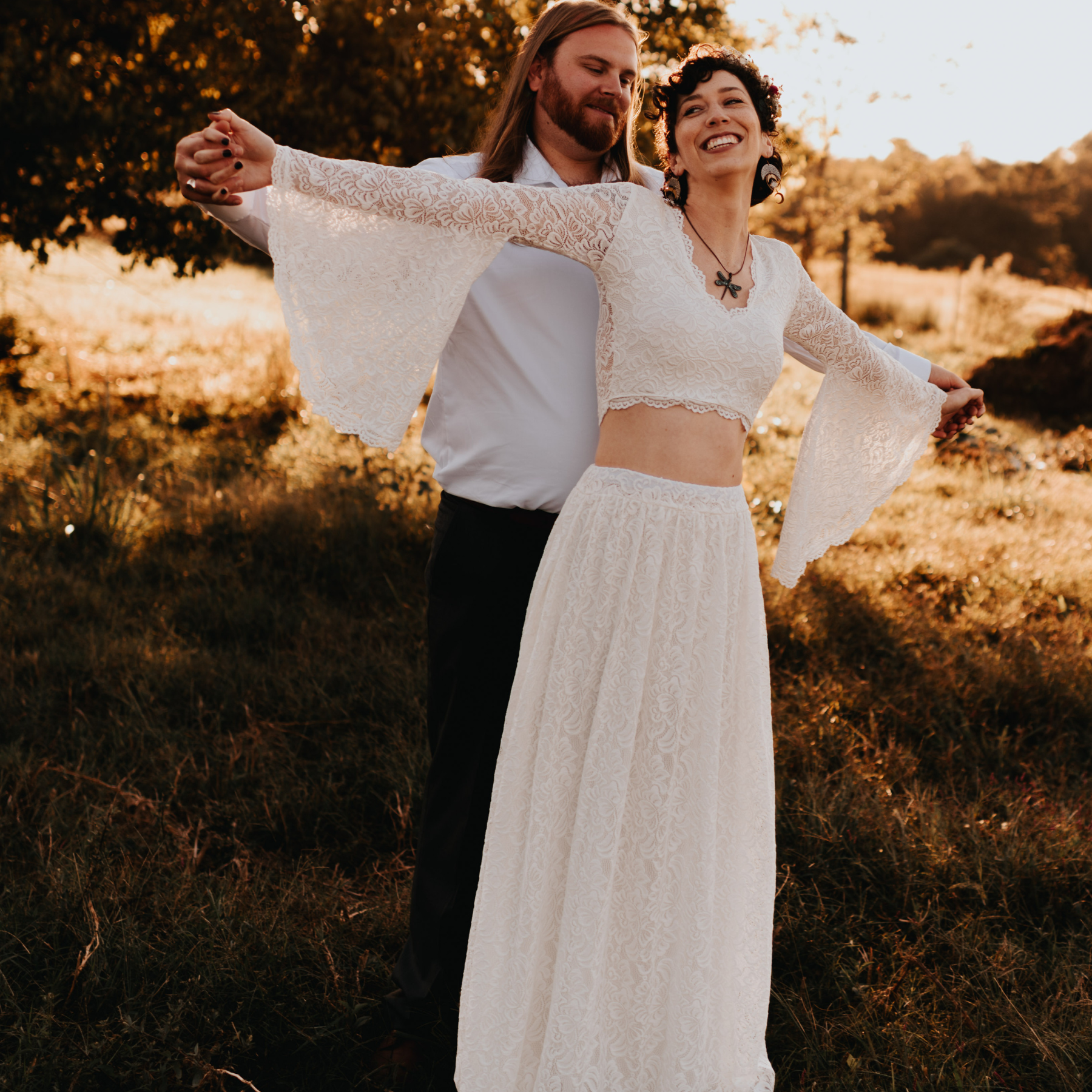 Bride in ivory lace Valvenia Bell Sleeve Bridal Top with bell sleeves, showcasing boho-chic elegance, embraces groom in nature.