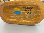 Bottom view of hand-painted wooden figurine showing "UKRAINE" inscription and painted flag colors, symbolizing craftsmanship.