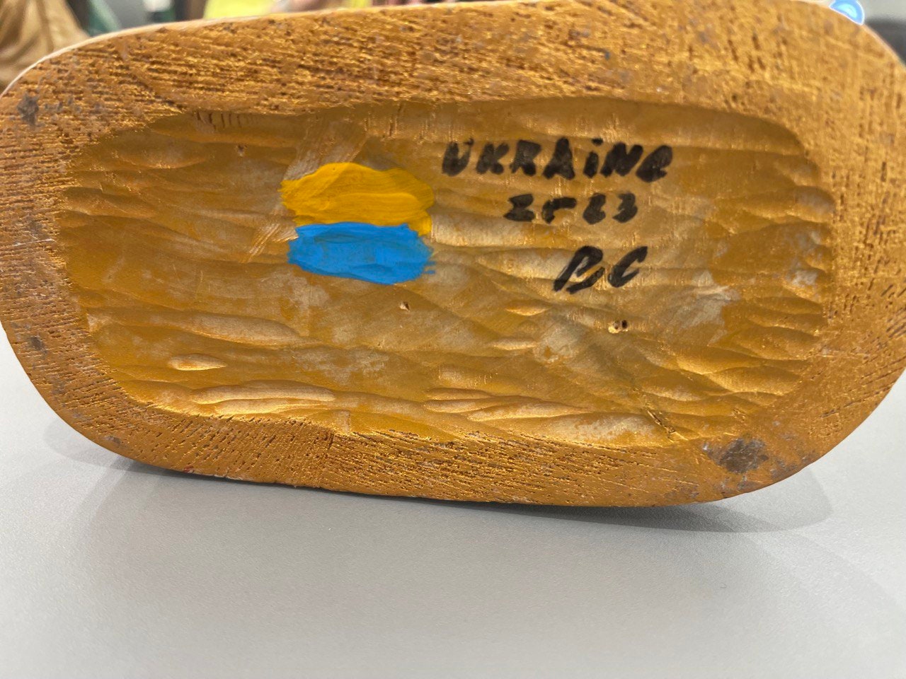 Bottom view of hand-painted wooden figurine showing "UKRAINE" inscription and painted flag colors, symbolizing craftsmanship.