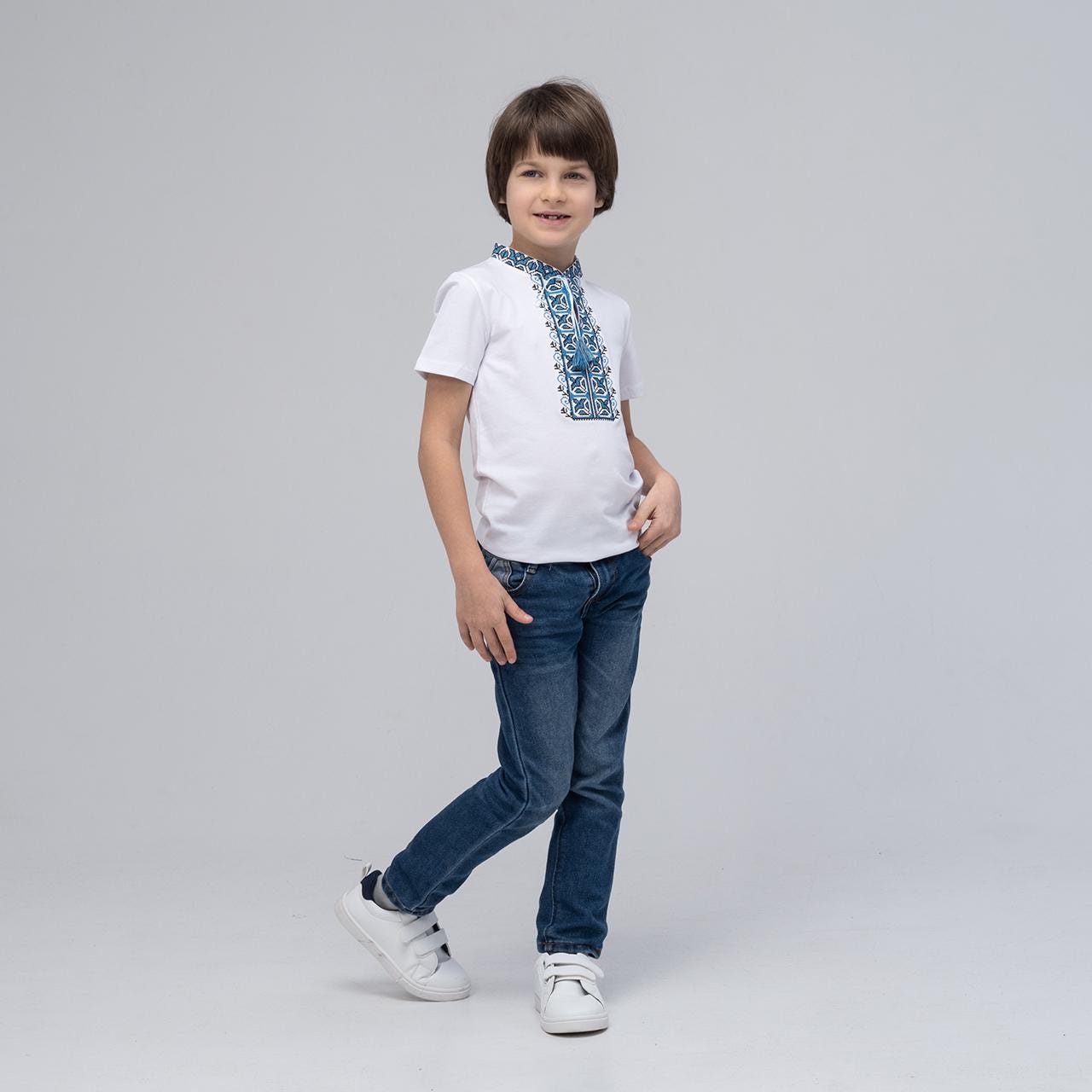 Boy wearing short sleeve blue embroidered Ukrainian vyshyvanka shirt with jeans, showcasing traditional and modern style.