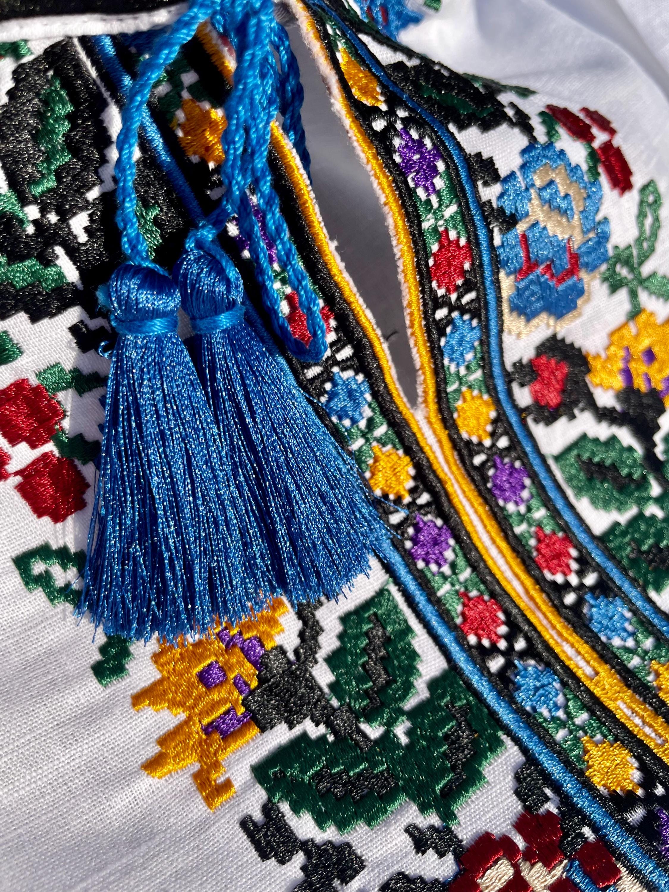Close-up of boys' embroidered linen shirt with Ukrainian vyshyvanka floral patterns and blue tassels.