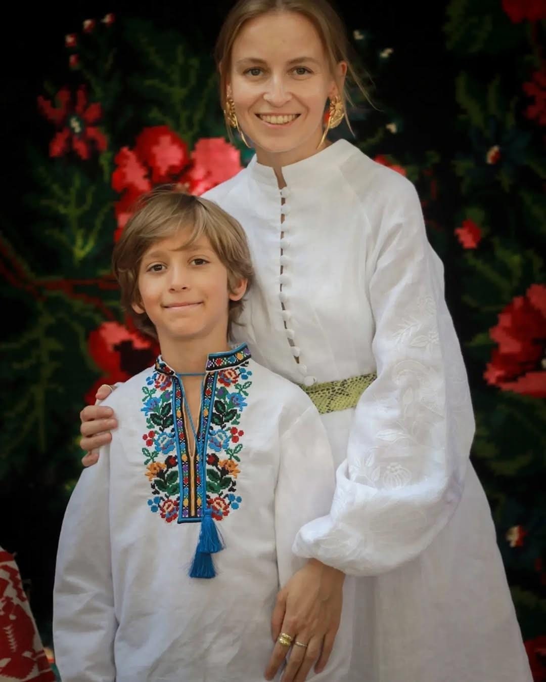 Boy wearing an embroidered Ukrainian vyshyvanka shirt with vibrant floral patterns, standing with a woman in traditional attire.