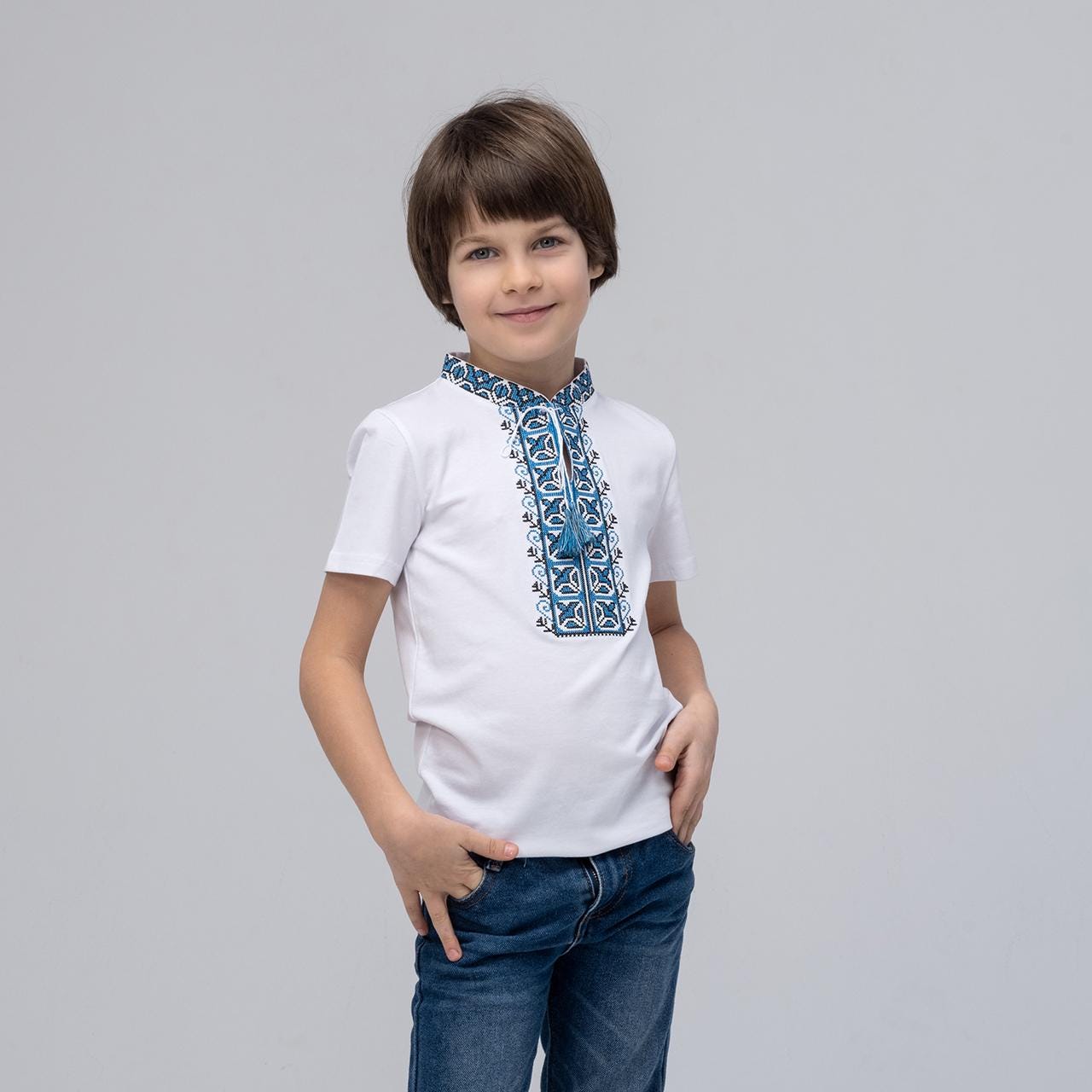 Boy wearing short sleeve Ukrainian embroidered shirt with blue ornament vyshyvanka, stand-up collar, side cuts, casual style.