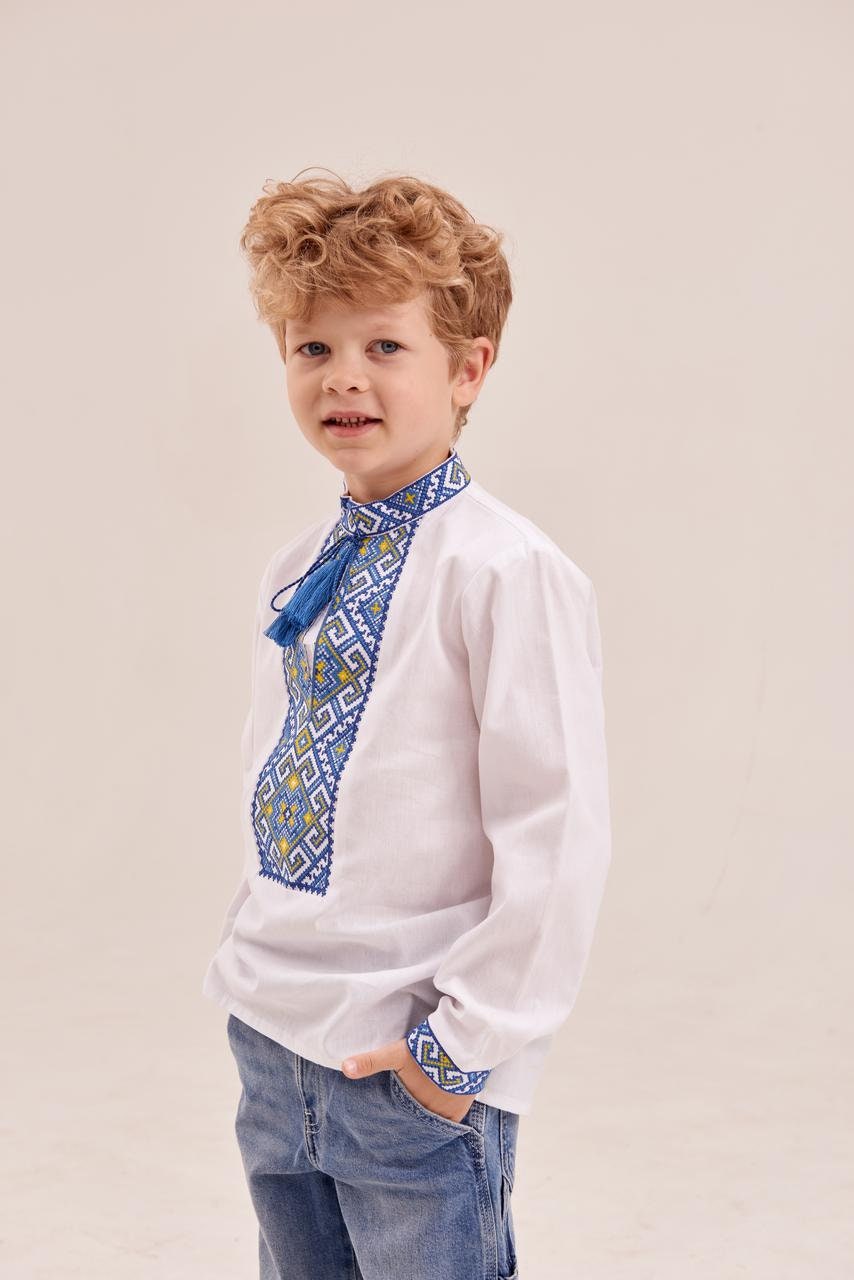 Boy wearing white Ukrainian embroidered shirt with blue ornament and tassels.