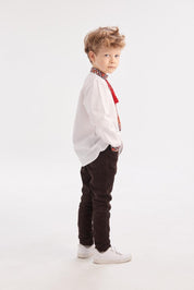 Young boy wearing a traditional white Ukrainian vyshyvanka shirt with red and black embroidery, paired with dark pants and white shoes.