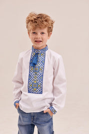 Young boy wearing a white Ukrainian embroidered shirt with blue and yellow geometric patterns, ideal for cultural events and festive occasions.