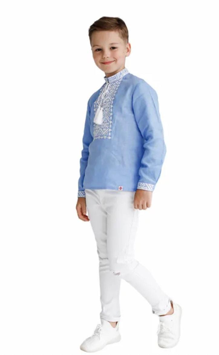 Boy wearing blue embroidered Ukrainian vyshyvanka shirt and white pants, showcasing traditional cross-stitch design.