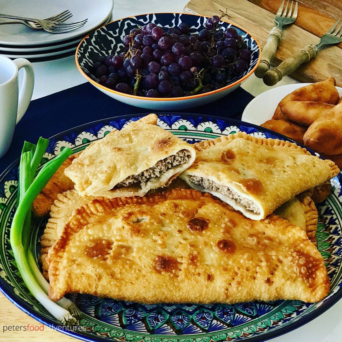 Homemade Ukrainian chebureki on a plate, featuring crispy dough and meat filling, served with fresh greens and fruit.