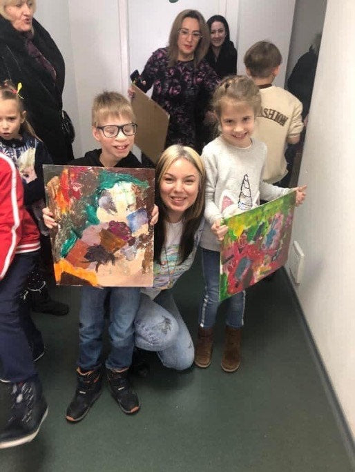 Children displaying colorful paintings with a smiling adult in a classroom setting.