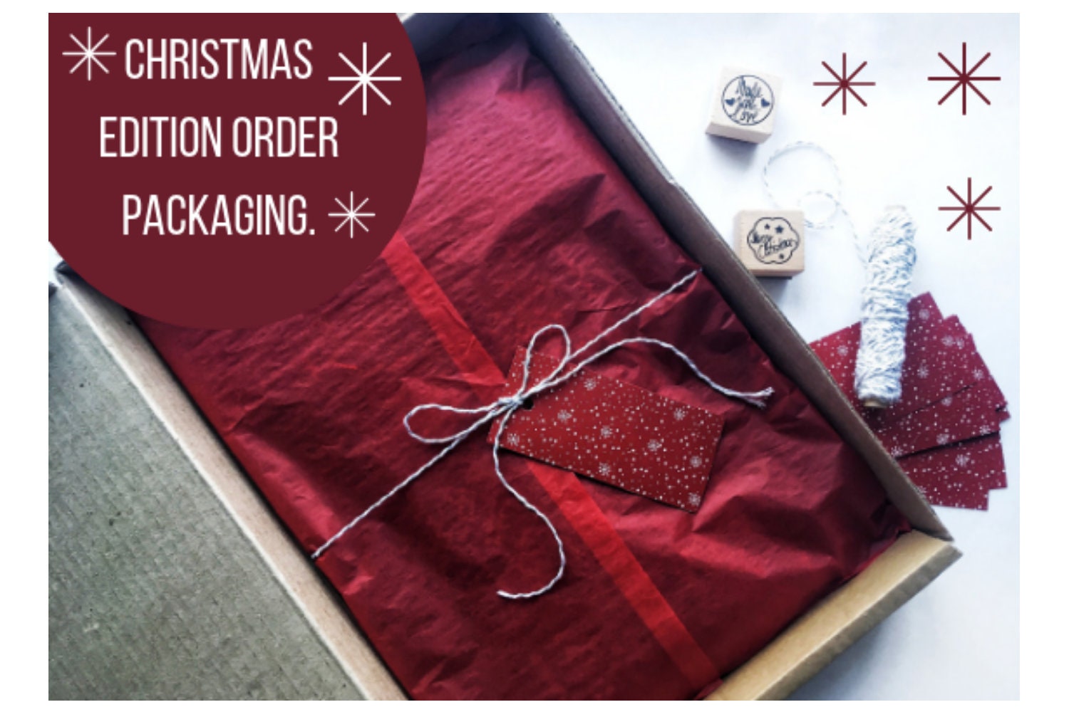 Christmas edition packaging with red wrapping, twine bow, and festive stamps in an open box.