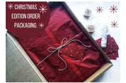 Christmas edition packaging with red wrapping, twine bow, and festive stamps in an open box.