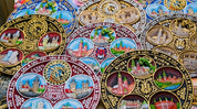 Colorful hand-painted souvenir plates displaying European city landmarks in intricate designs.