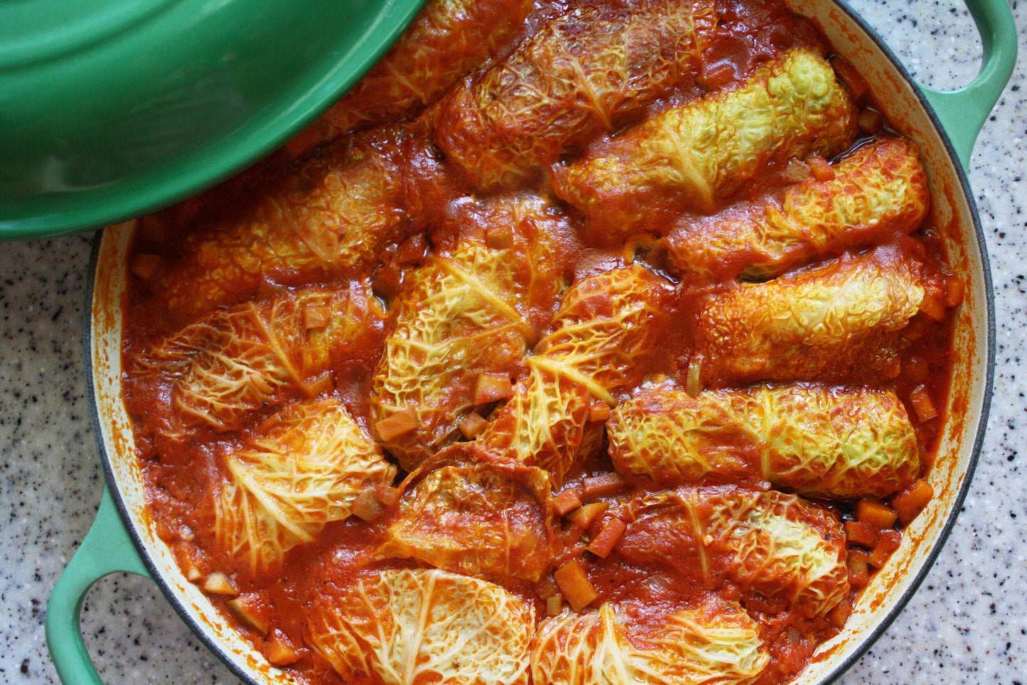 Homemade Ukrainian holubtsi stuffed cabbage rolls in a green dish with rich tomato sauce, highlighting traditional flavors and cooking style.