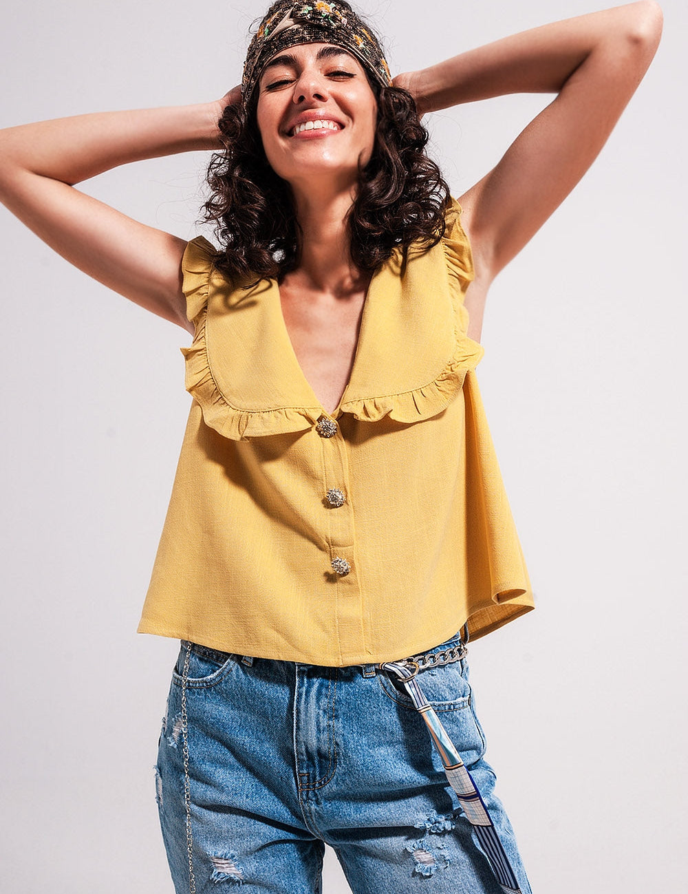 Woman wearing a sleeveless yellow crop top with a bib collar and frill trim, styled with denim jeans, exuding summer charm.