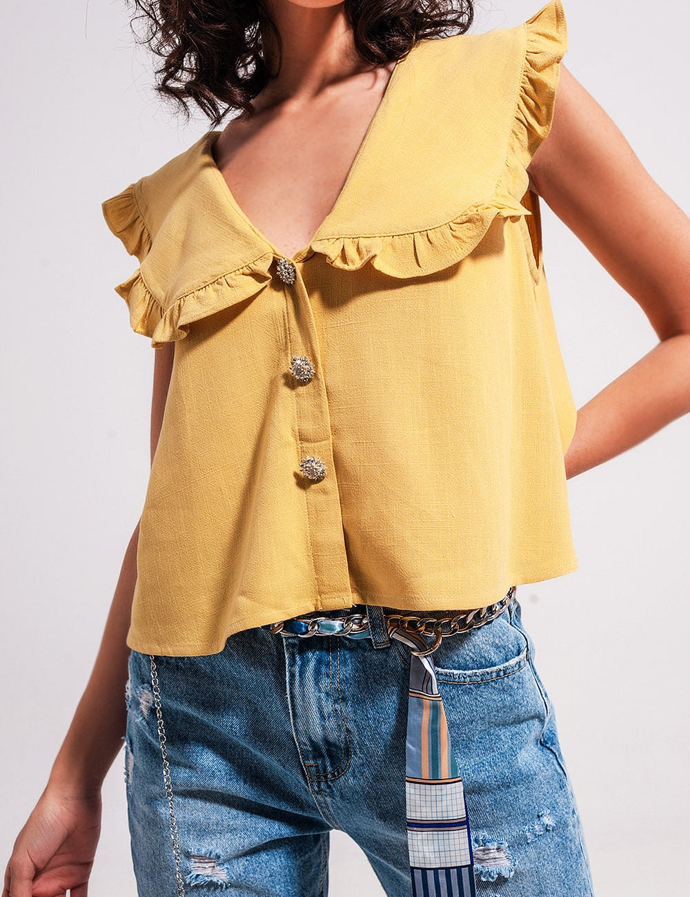 Sleeveless yellow crop top with bib collar, button placket, and frill trim, styled with blue jeans for a summer look.