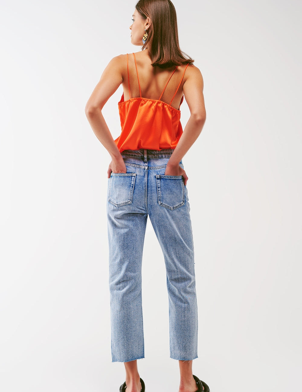 Woman wearing fiery orange satin open-back crop top with spaghetti straps and blue jeans, displaying a modern chic ensemble for summer soirées.