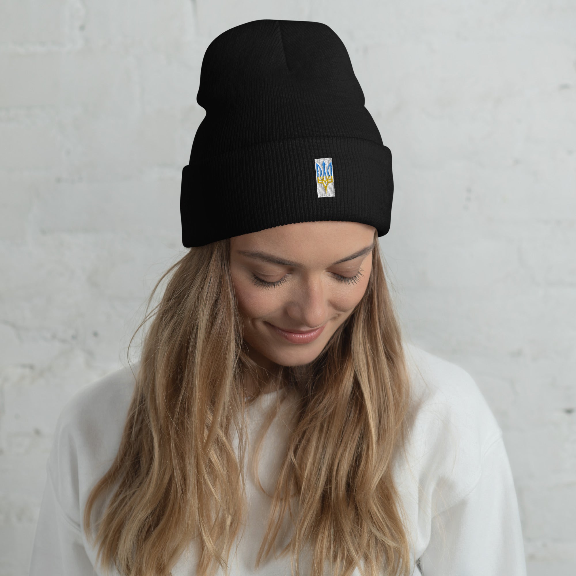Woman wearing a black unisex cuffed beanie with Ukrainian Tryzub emblem, showcasing blue and yellow embroidered design.