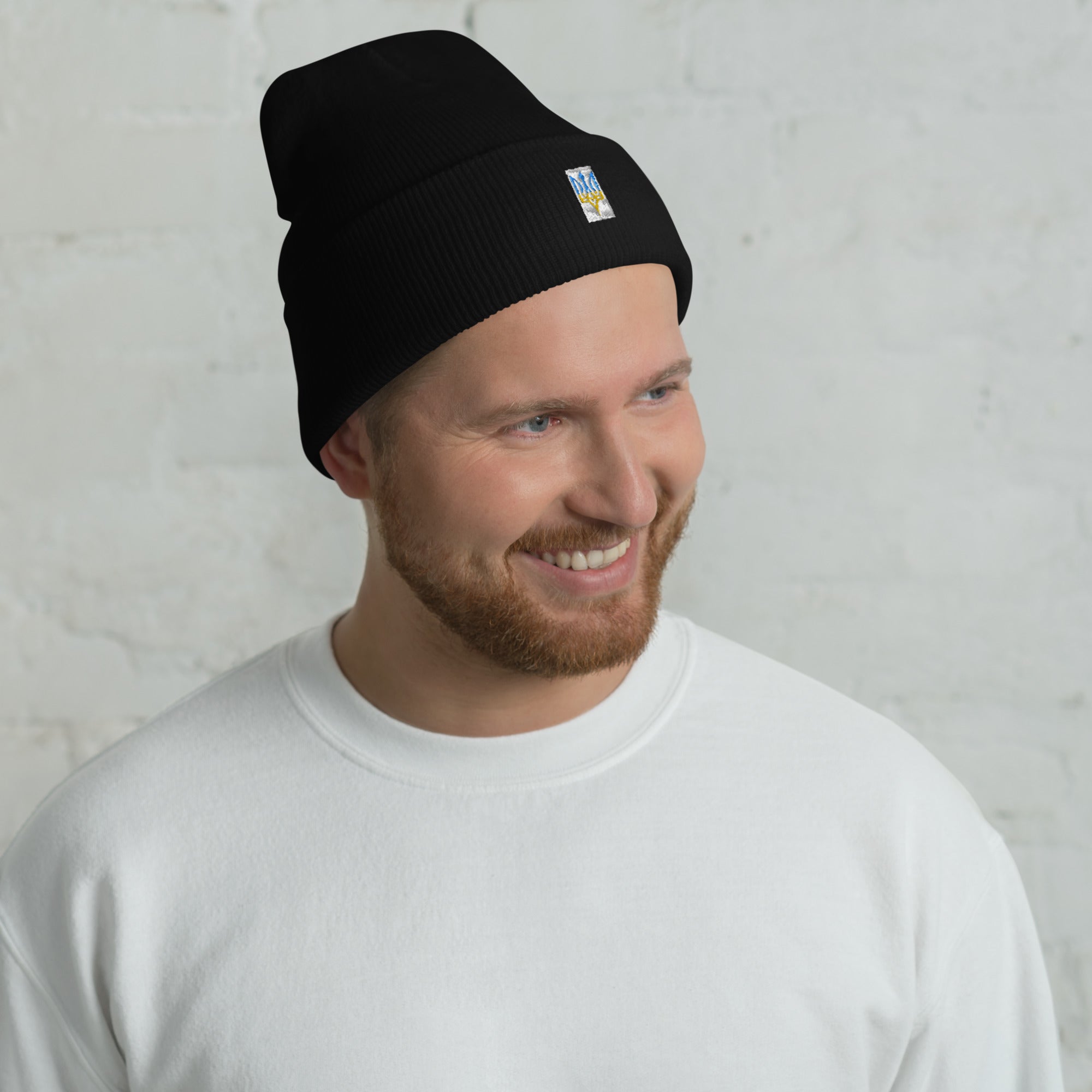 Unisex cuffed beanie with embroidered Ukrainian Tryzub emblem, worn by a smiling man in a white shirt.
