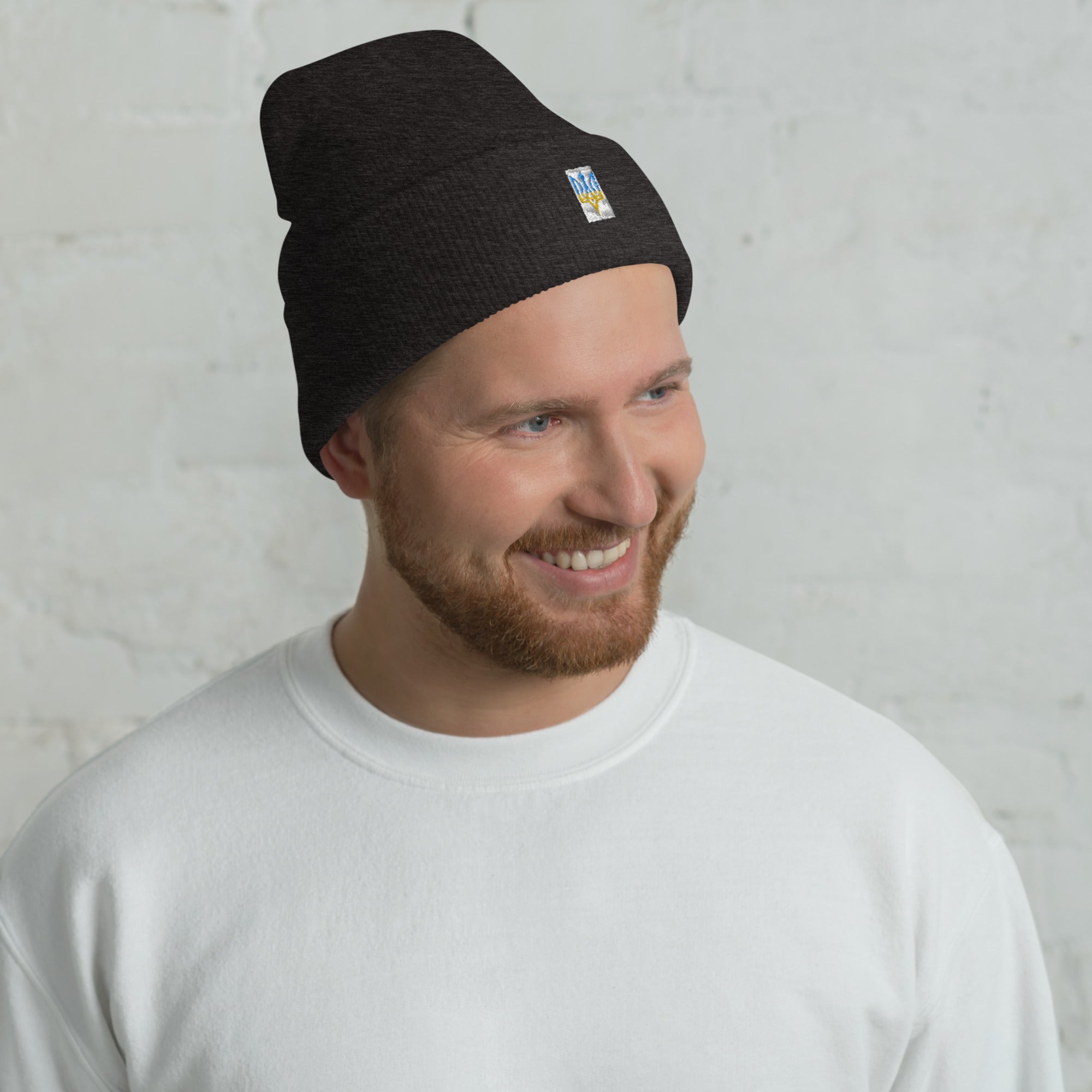 Man wearing unisex cuffed beanie with Ukrainian Tryzub emblem, smiling against a light background.