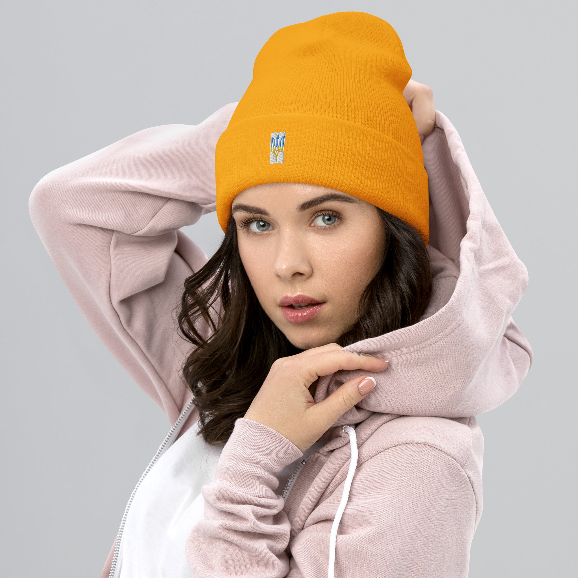 Woman wearing an orange unisex cuffed beanie with Ukrainian Tryzub emblem, styled with a pink hoodie for a trendy look.
