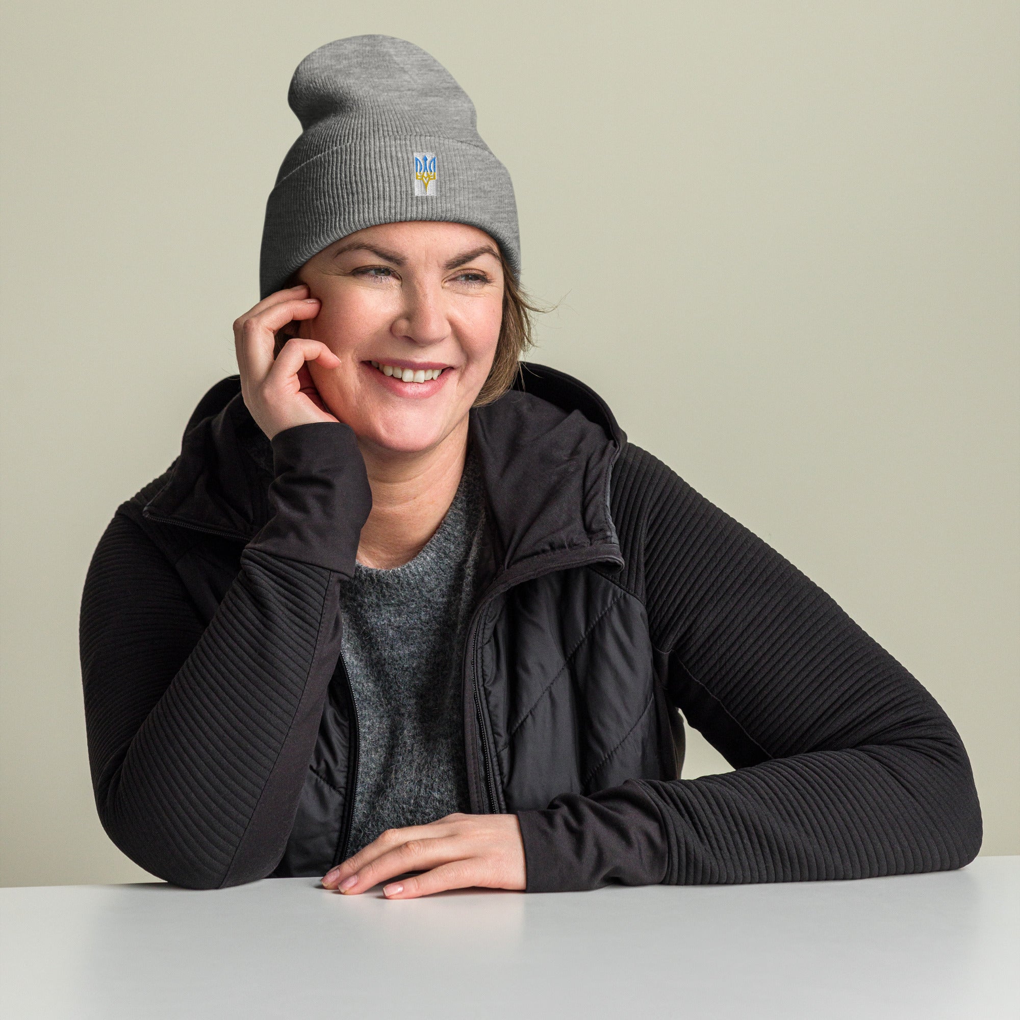 Woman wearing gray unisex cuffed beanie with Ukrainian Tryzub embroidery, smiling and sitting at a table.