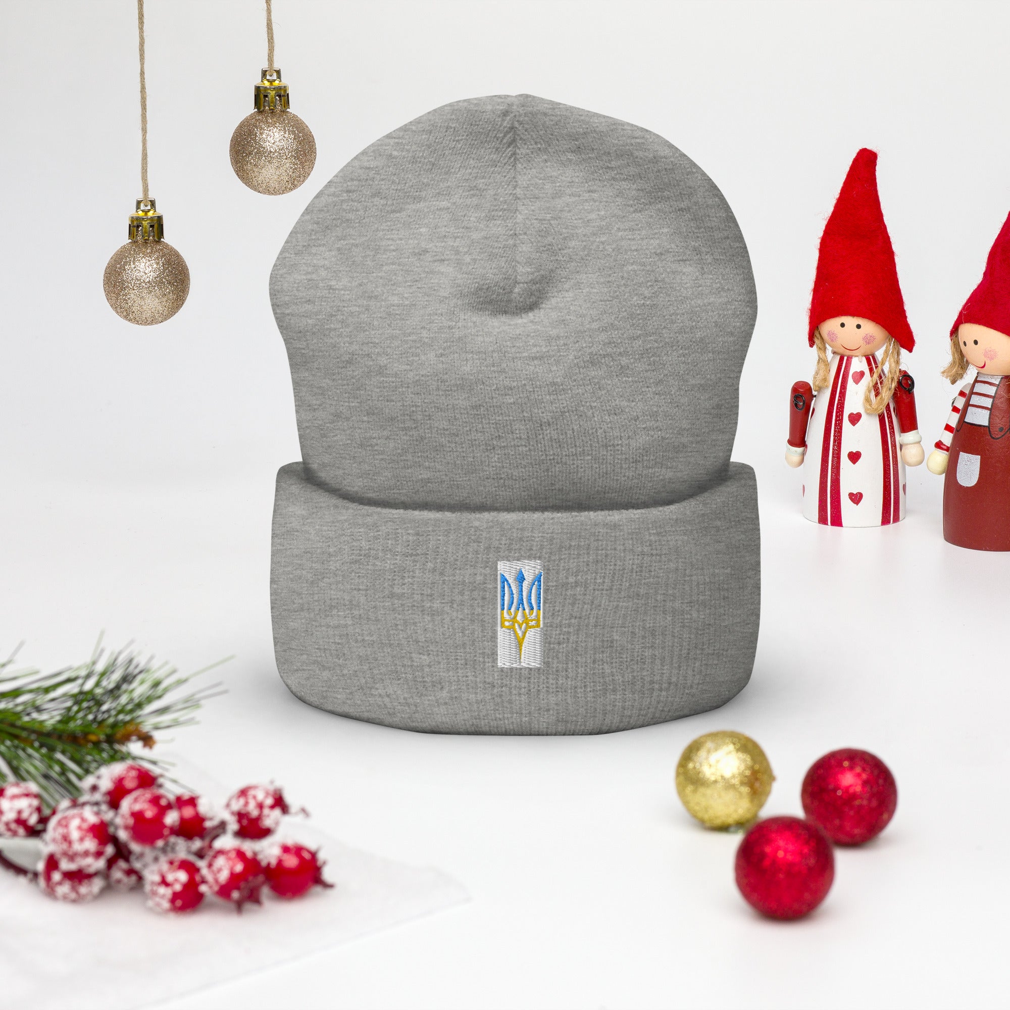 Gray unisex cuffed beanie with embroidered blue and yellow Ukrainian Tryzub emblem, surrounded by festive holiday decor.