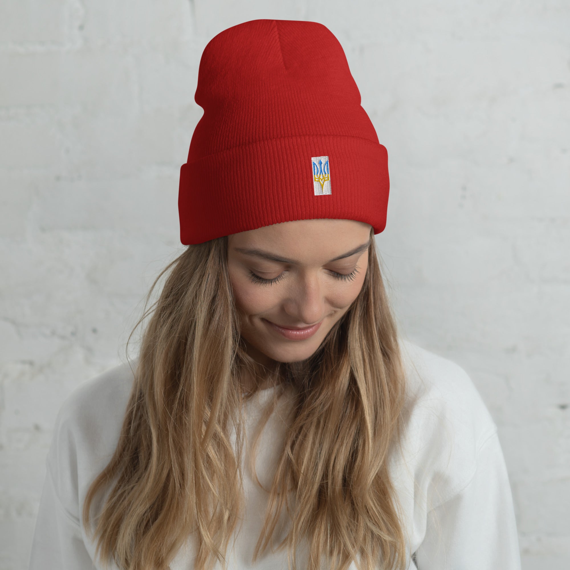Unisex red cuffed beanie with Ukrainian Tryzub emblem, worn by a smiling person against a white background.