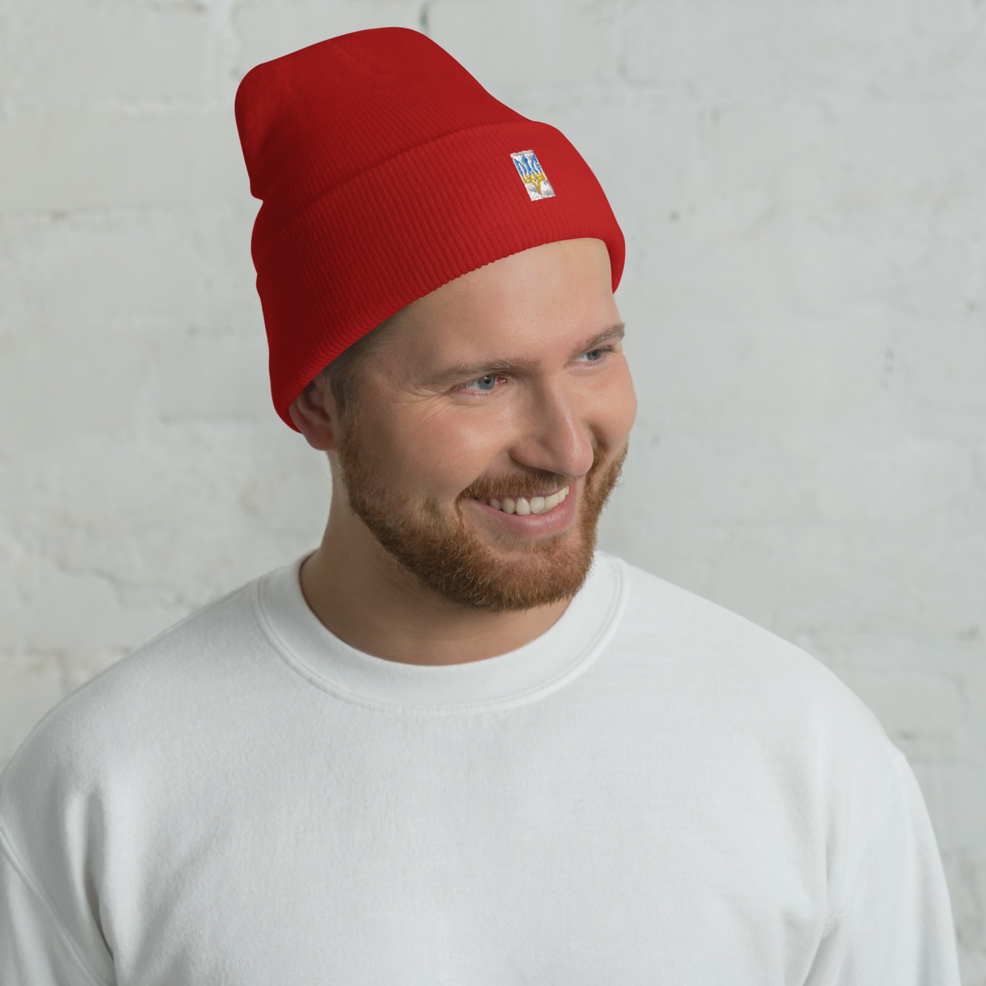 Person wearing red cuffed beanie with embroidered patch, smiling against a white background.