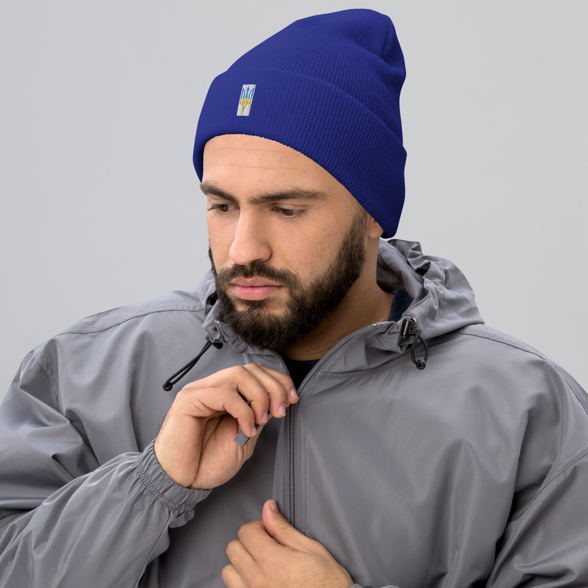 Unisex blue cuffed beanie with embroidered Ukrainian Tryzub emblem, worn with a grey jacket, showcasing style and Ukrainian pride.