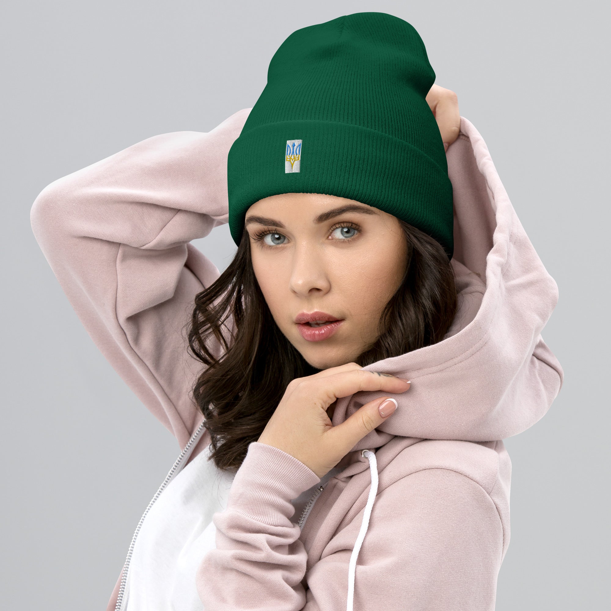 Unisex green cuffed beanie with embroidered Ukrainian Tryzub emblem worn by a woman in a pink hoodie.