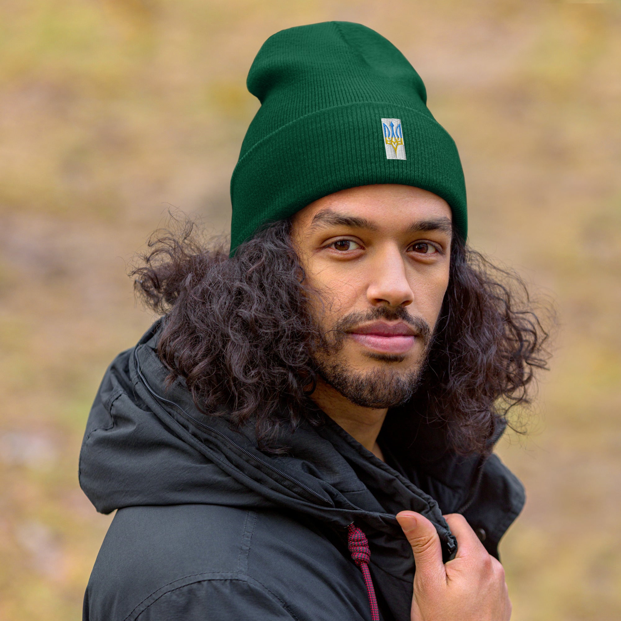 Man wearing green cuffed beanie with embroidered Ukrainian Tryzub emblem outdoors, showcasing warmth and style.