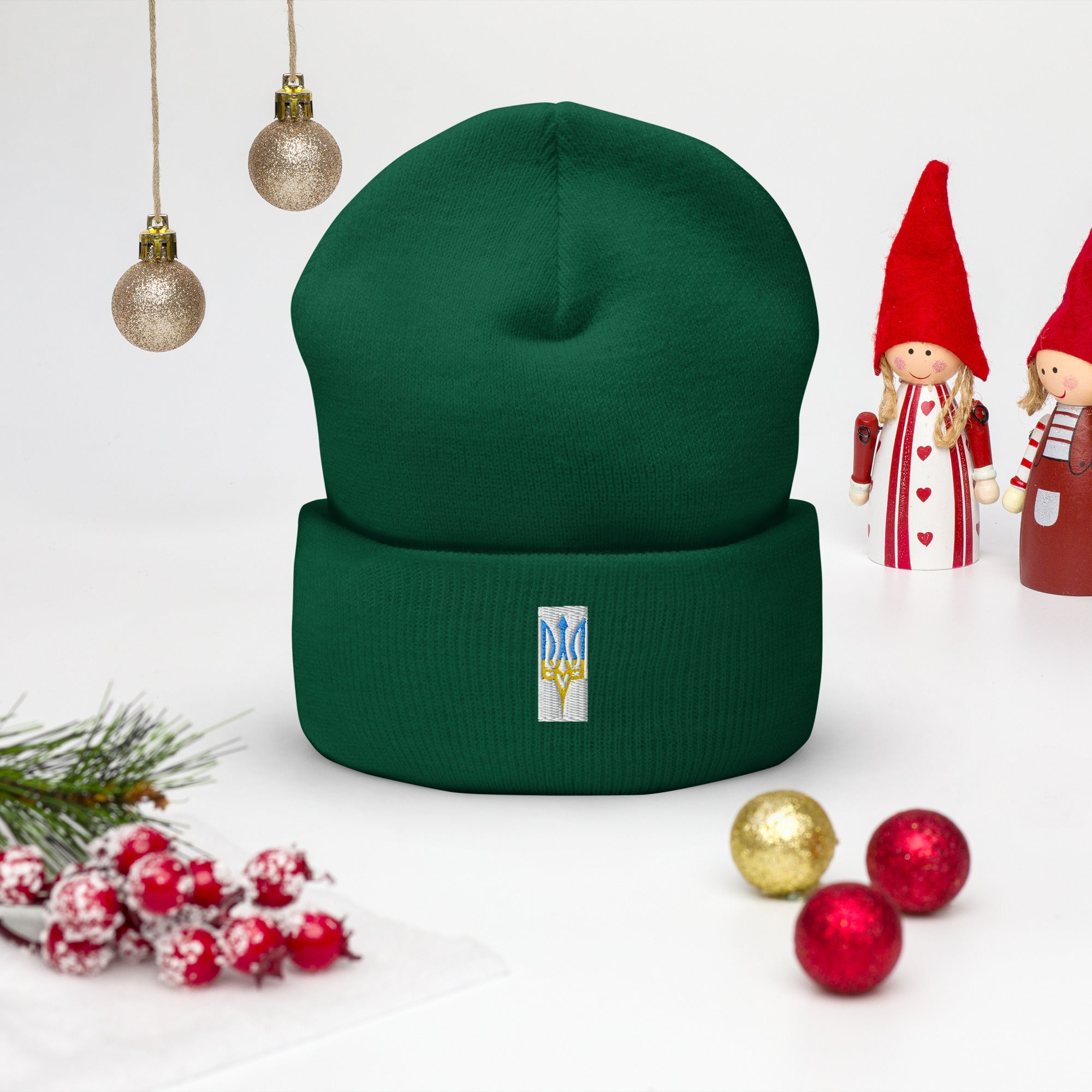 Green unisex cuffed beanie with embroidered Ukrainian Tryzub emblem, surrounded by holiday decorations.