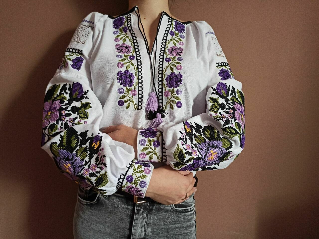 Woman wearing custom Ukrainian Vyshyvanka blouse with purple floral embroidery on white fabric.