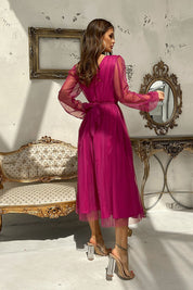 Woman wearing pink mesh-layered evening midi dress with sheer sleeves, standing in a stylish room with vintage decor and mirrors.