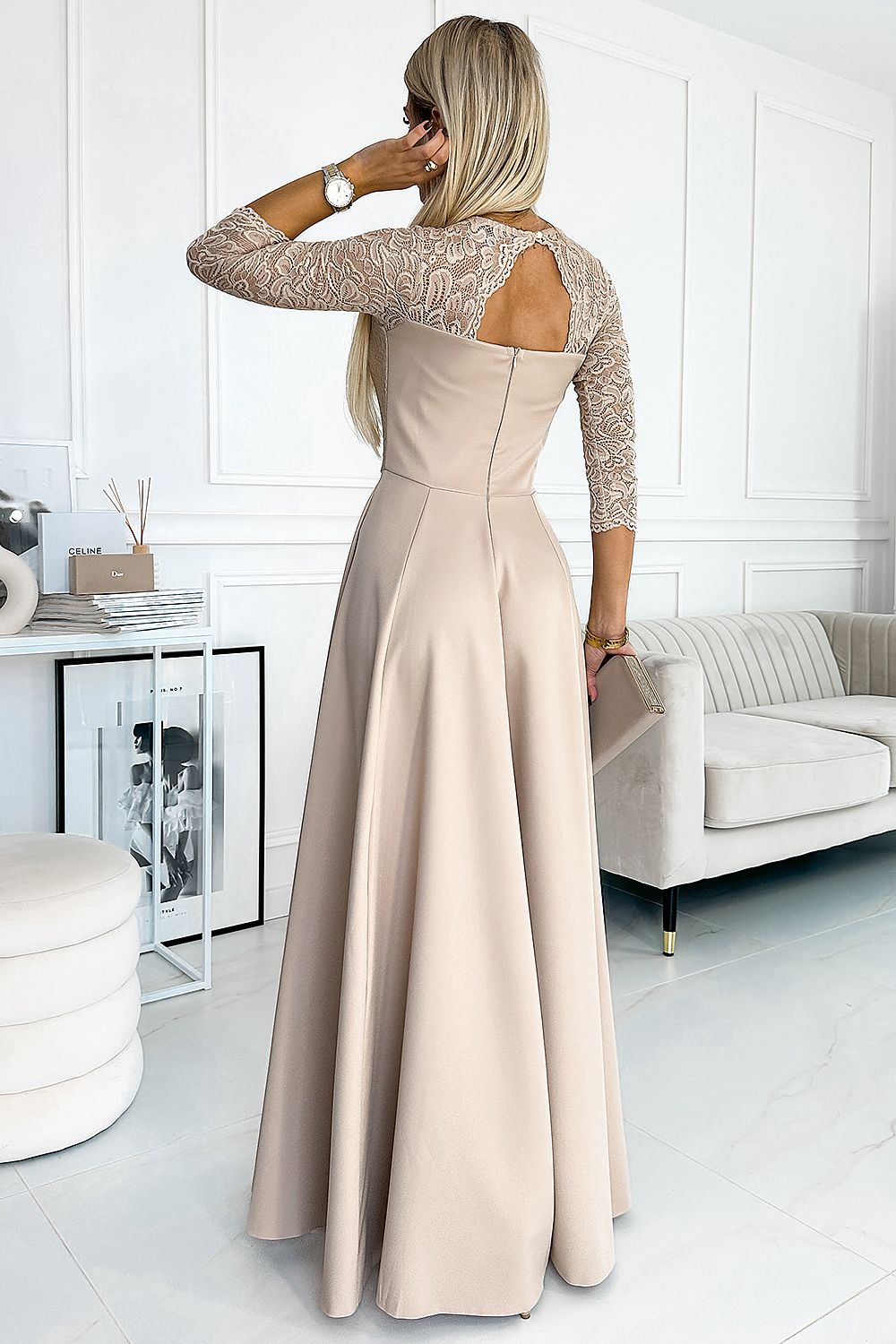 Woman wearing Alviera Beige Lace Maxi Gown with open back design, standing in elegant room setting.