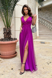 Woman in a vibrant purple evening gown with a deep V-neck and high slit, standing near stairs and a large pot plant.