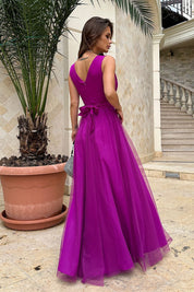 Elegant woman in a striking purple evening dress with a bow, standing outdoors next to a potted palm.